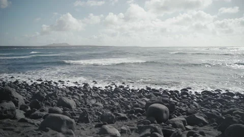 Old volcano in the distance, stone beach with sea waves, cloudy and windy day Stock Footage 235679879