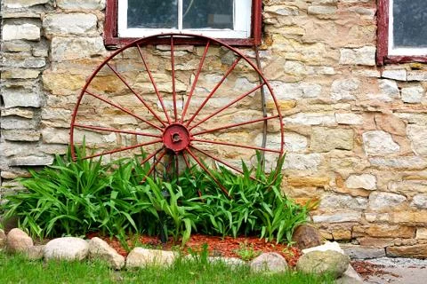 Old wagon wheel in front of stone barn Stock Photos