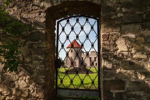 Old wall and tower through iron grid. Ruins of the ancient castle in old town of Stock Photos