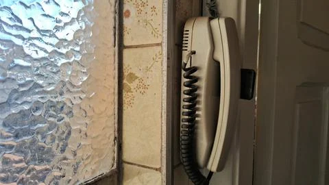 Old wall mounted telephone with coiled cord beside patterned glass window Stock Photos