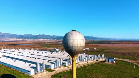 Old water tower of spherical shape. Large farm complex of numerous warehouses at Stock Footage 328372945
