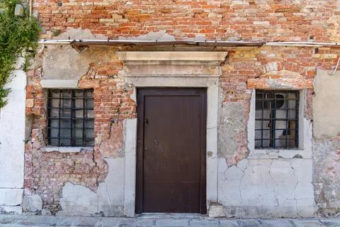 Old weathered brick wall with rustic door and windows. Aged brick and plaster Stock Photos