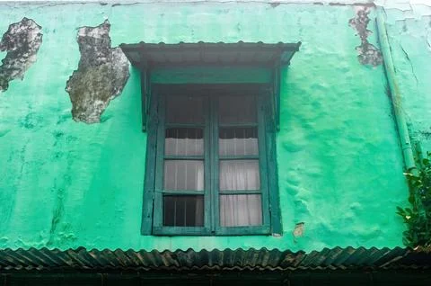 An old, weathered green wall with a rustic window and a small awning. The p.. Stock Photos