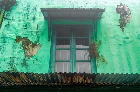 An old, weathered green wall with a rustic window and a small awning. The p.. Stock Photos