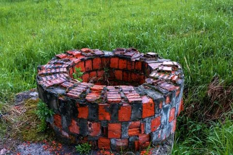 Old well of red brick on a background of green grass. Stock Photos