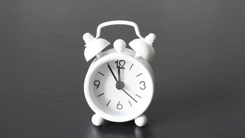 Old white alarm clock with black numbers and arrows on a black background Stock Footage 114687924