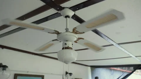 Old white ceiling fan with electric lamp spinning and cooling air during the Stock Footage 259886323