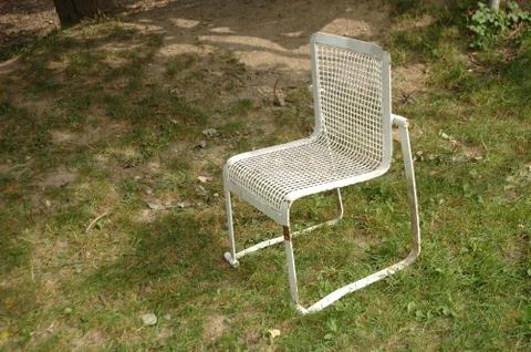 Old white iron rusty empty chair standing on grass Stock-Fotos