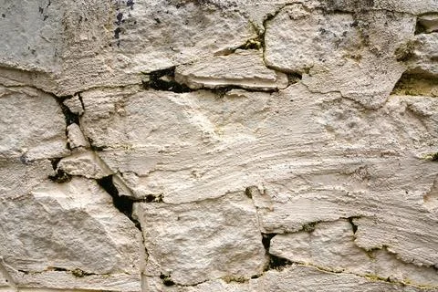 Old white stone wall texture with deep cracks and green moss growth backgroun Stock Photos