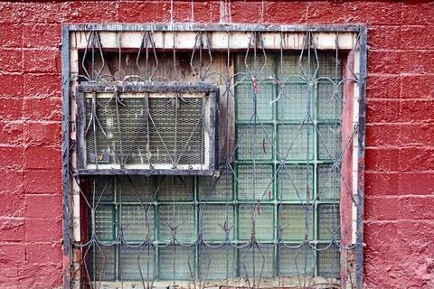 Old window with air conditioner unit and rusty metal security bars on red bricks Stock Photos