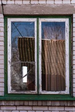 An old window with a cracked pane held together with tape in an abandoned hou Stock Photos