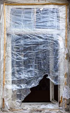 Old window frame cracked, wrapped in plastic on stone building Stock Photos