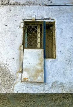 Old window with metal security bars and hatch door on a textured concrete wall 库存照片