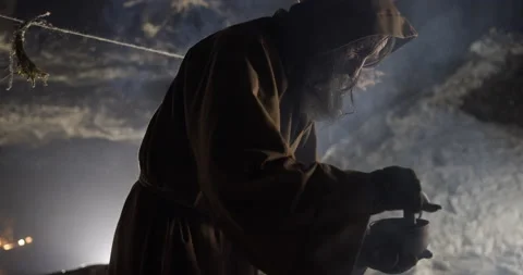 Old wizard brews potion mixing with spoon in bowl in cave Stock Footage 168808538