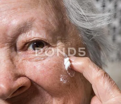 Old woman applying anti-aging cream Stock Photos