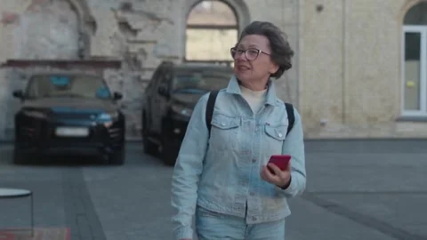Old woman browsing maps using smartphone in city districts outdoors. An Stock Footage 257670801