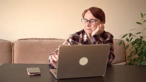An old woman of eighty years old sits with a laptop Stock Footage 253184067