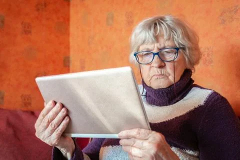 Old woman holding digital tablete in hands at home Stock Photos