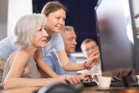 Old woman learning computer programs with teacher in training room Foto stock