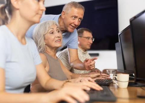 Old woman learning computer programs with teacher in training room Fotos de archivo