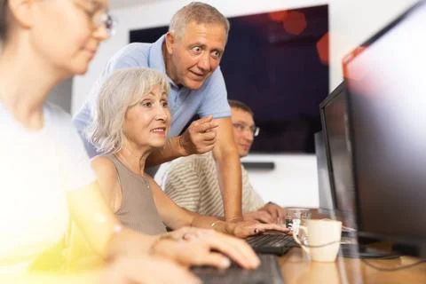 Old woman learning computer programs with teacher in training room Stock Photos