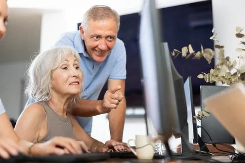 Old woman learning computer programs with teacher in training room Foto stock