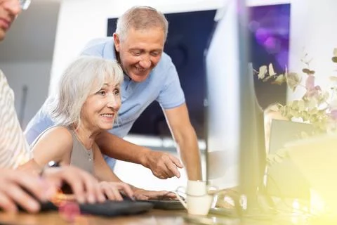 Old woman learning computer programs with teacher in training room Foto stock