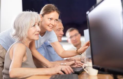 Old woman learning computer programs with teacher in training room Fotos de archivo