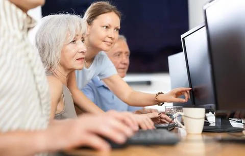 Old woman learning computer programs with teacher in training room Foto stock