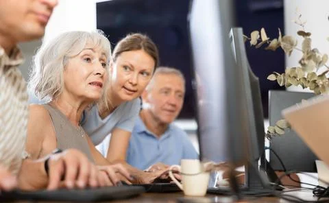Old woman learning computer programs with teacher in training room Foto stock