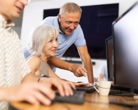 Old woman learning computer programs with teacher in training room Stock Photos