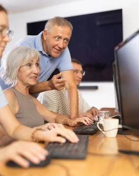 Old woman learning computer programs with teacher in training room Stock Photos