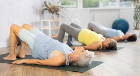 Old woman practicing bridge pose of yoga in training room during fitness classes Stock Photos