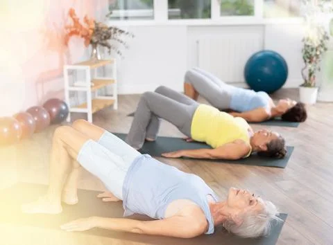 Old woman practicing bridge pose of yoga in training room during fitness classes Stock Photos