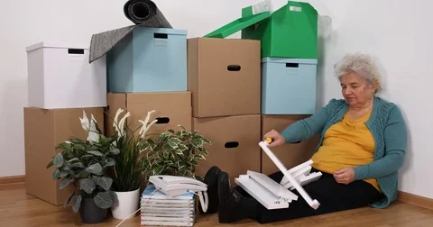 Old Woman Sit Matching Pieces of Furniture with Screwdriver on Floor in New Home Stock Footage