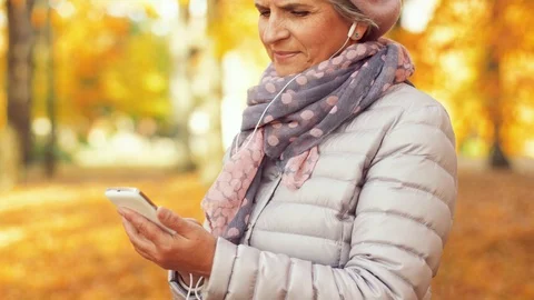 Old woman with smartphone and earphones in autumn Stock Footage