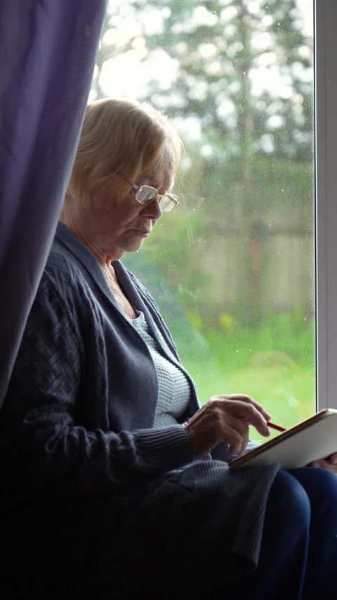 Old woman using digital tablet sitting near window Stock Footage 316607229