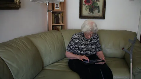 Old woman using a tablet computer on couch, disabled elderly female, Internet Stock Footage 36544406