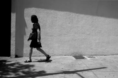 Old woman walks on the street under sun and shadow Stock Photos