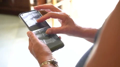 Old woman watching her x-ray on mobile phone at home, virtual doctor concept. Stock Footage 158546053