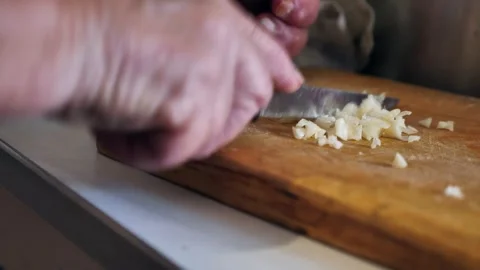 An old woman's hands finely chopping garlic with a knife on an old wooden board Stock Footage 339302370