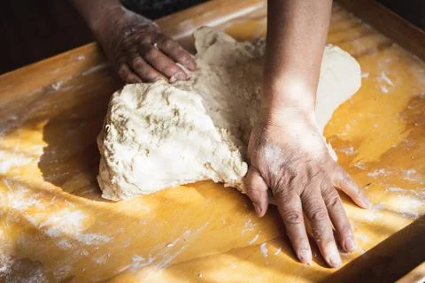Old woman's hands kneading bread dough. Empanadas. Wooden table. Stock Photos