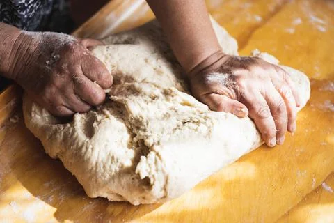 Old woman's hands kneading bread dough. Empanadas. Wooden table. Stock Photos