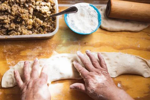 Old woman's hands kneading bread dough. Empanadas. Wooden table. Stock Photos