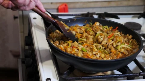An old woman's hands prepare vegetable stew in a frying pan on a gas stove. Stock Footage 339300739