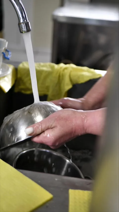 Old woman's hands washing and rinsing dishes by hand under running water in a Stock Footage 306326802
