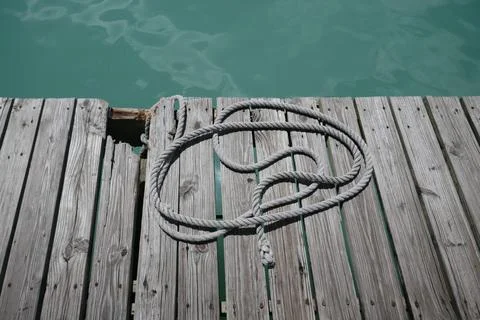 Old wooden boat dock with rope by ocean water Stock Photos