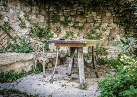 Old wooden table and patterned metal chair near the stone Stock Photos