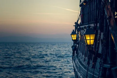 Old wooden vintage pirate ship on sea water surface in sunset evening romanti Stock Photos