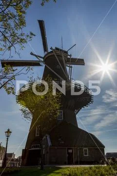 Old wooden windmill on top of structure with sunburst and blue sky Stock Photos
